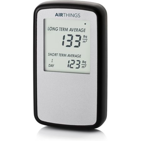 Moniteur Airthings Corentium Home : boîtier blanc allongé tenu à la verticale, son petit écran affichant des chiffres dans la partie supérieure, sur fond clair